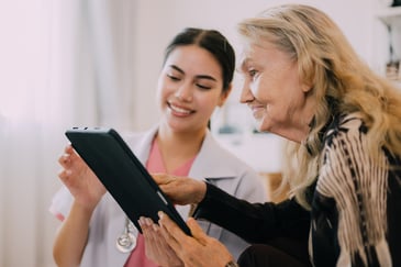 A healthcare professional viewing a tablet with patient analytics, while smiling and talking with a patient.